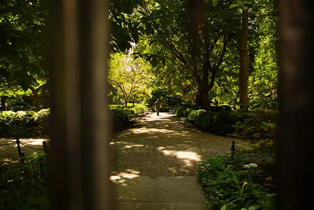 A view through the gates of Gramercy Park with a keyholder to the private park seen in the background strolling beneath trees.